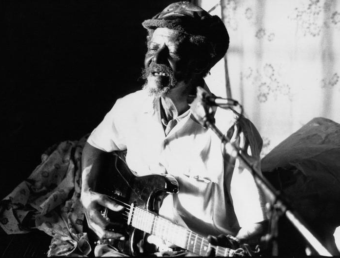 Cecil Barfield plays the guitar and sings into a microphone with closed eyes.